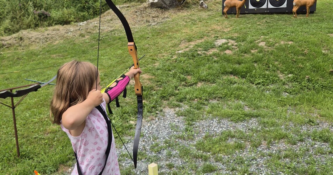 Kind beim Bogenschießen auf einer Wiese mit Zielscheiben im Hintergrund. | © Bogensport Vorderegger