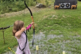 Kind beim Bogenschießen auf einer Wiese mit Zielscheiben im Hintergrund. | © Bogensport Vorderegger