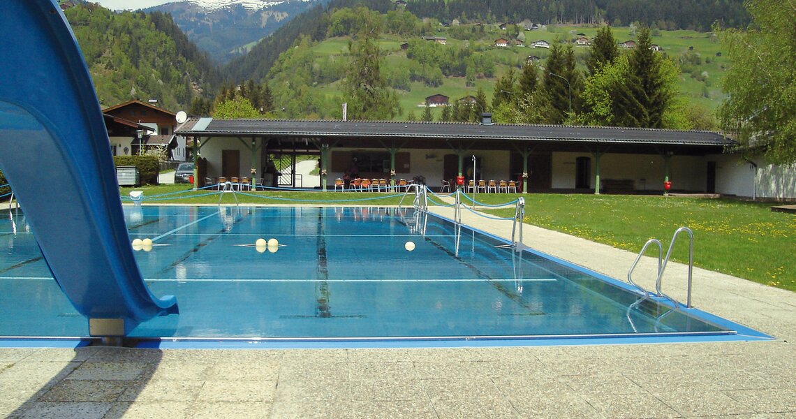 Freibad mit blauem Pool und Rutsche, umgeben von grünen Hügeln und Bergen. | © Schwimmbad Mühlbach im Pinzgau
