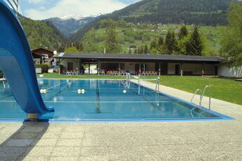 Freibad mit blauem Pool und Rutsche, umgeben von grünen Hügeln und Bergen. | © Schwimmbad Mühlbach im Pinzgau