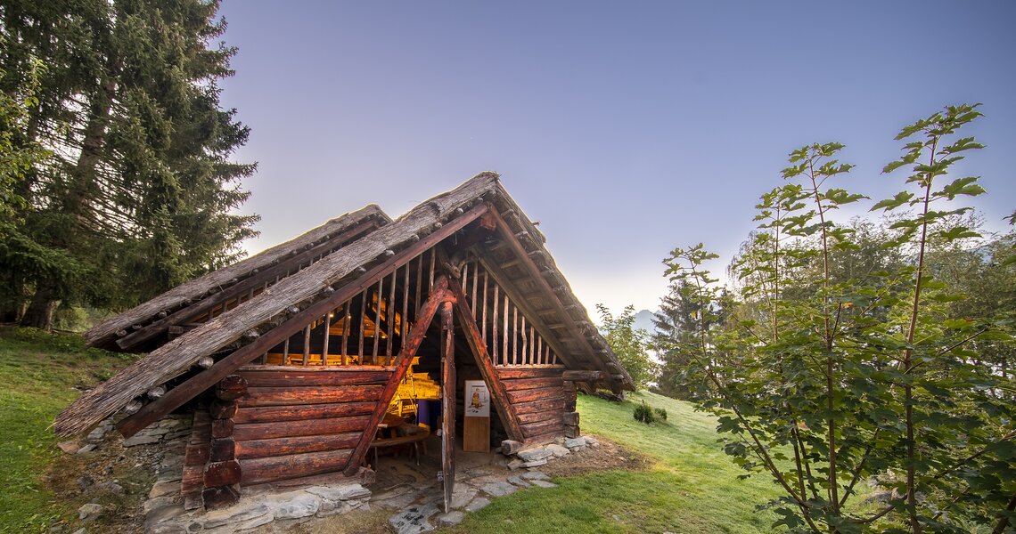 Historisches Holzhaus in traditioneller Bauweise bei Sonnenuntergang, umgeben von Bäumen. | © Keltendorf am Stoanabichl Uttendorf