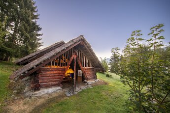 Historisches Holzhaus in traditioneller Bauweise bei Sonnenuntergang, umgeben von Bäumen. | © Keltendorf am Stoanabichl Uttendorf