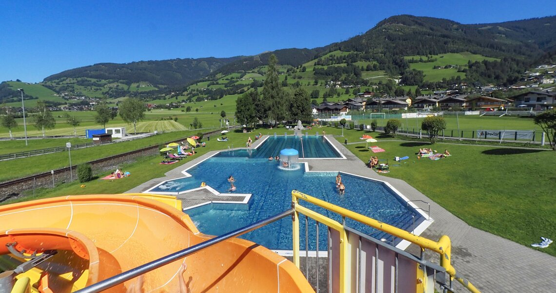 Außenpool mit Wasserrutsche und umliegender Berglandschaft an einem sonnigen Tag. | © Hinkelsteibad Piesendorf