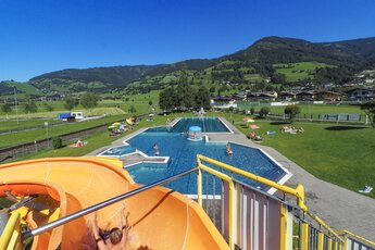 Außenpool mit Wasserrutsche und umliegender Berglandschaft an einem sonnigen Tag. | © Hinkelsteibad Piesendorf