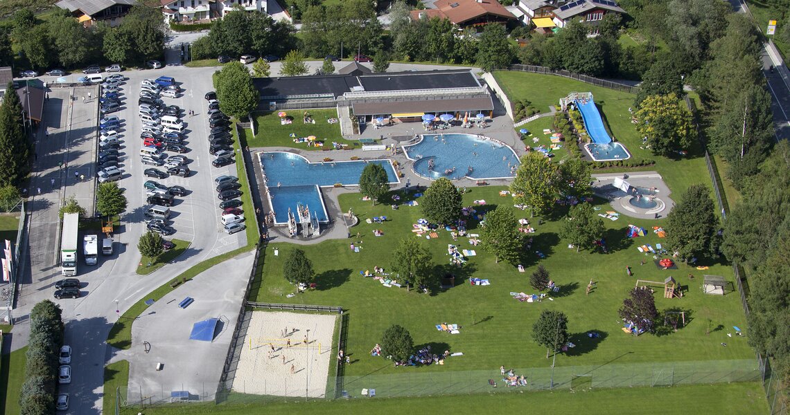Luftaufnahme eines Freibads mit mehreren Pools, Liegewiese und umliegenden Häusern. | © Freischwimmbad Mittersill