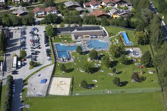 Luftaufnahme eines Freibads mit mehreren Pools, Liegewiese und umliegenden Häusern. | © Freischwimmbad Mittersill