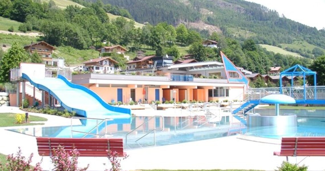 Freibad mit blauer Rutsche und modernem Gebäude, eingebettet in die grüne Landschaft der Berge. | © Freibad Stuhlfelden
