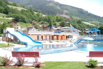 Freibad mit blauer Rutsche und modernem Gebäude, eingebettet in die grüne Landschaft der Berge. | © Freibad Stuhlfelden