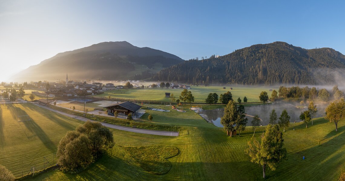 Panoramablick auf eine Freizeitanlage mit See, Sportfeldern und Bergen im Hintergrund. | © Freizeitanlage Hollersbach