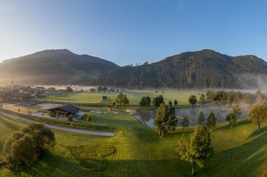 Panoramic view of a leisure facility with a lake, sports fields, and mountains in the background. | © Freizeitanlage Hollersbach