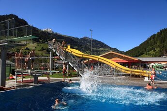 Freibad mit gelber Wasserrutsche, Sprungturm und Besuchern, umgeben von Bergen und grüner Natur. | © Freibad Großarl