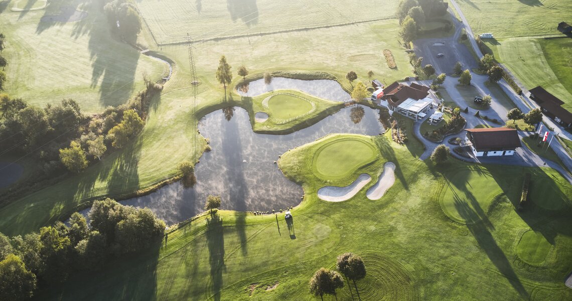 Luftaufnahme eines gepflegten Golfplatzes mit Teichen und umliegendem Grün bei Sonnenaufgang. | © Golfclub Nationalpark Hohe Tauern
