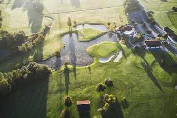Luftaufnahme eines gepflegten Golfplatzes mit Teichen und umliegendem Grün bei Sonnenaufgang. | © Golfclub Nationalpark Hohe Tauern