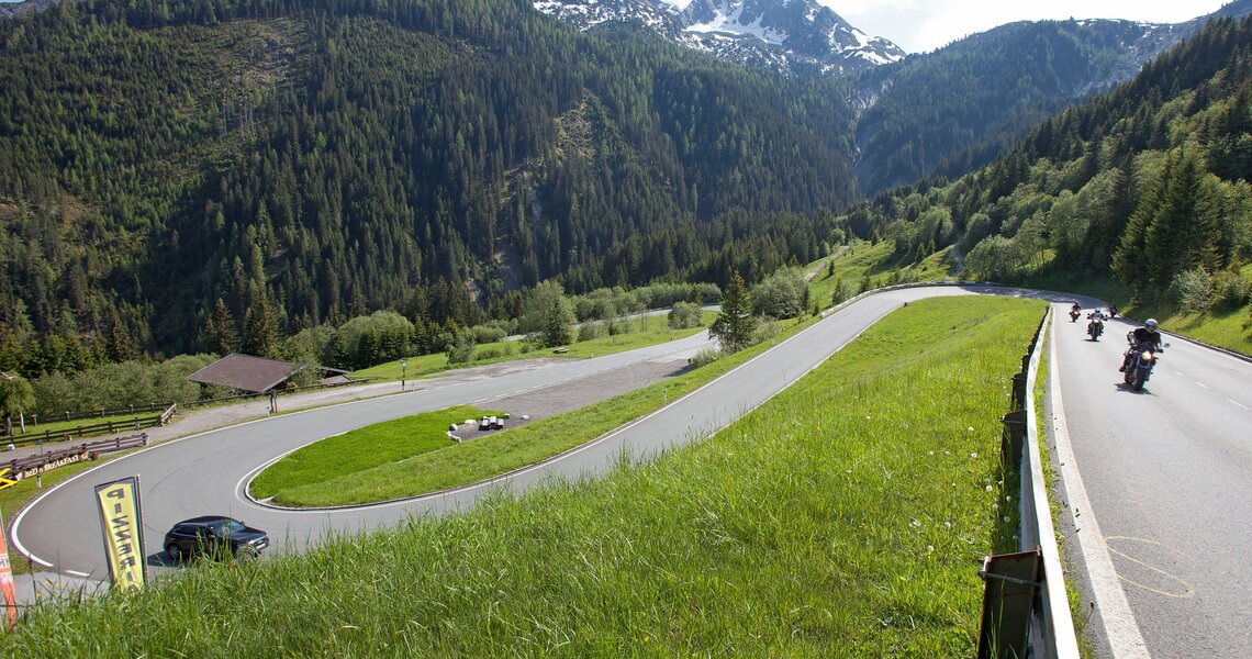Winding mountain road through forested hills with motorbikes and cars on a sunny day. | © Kassenstelle Gerlospass