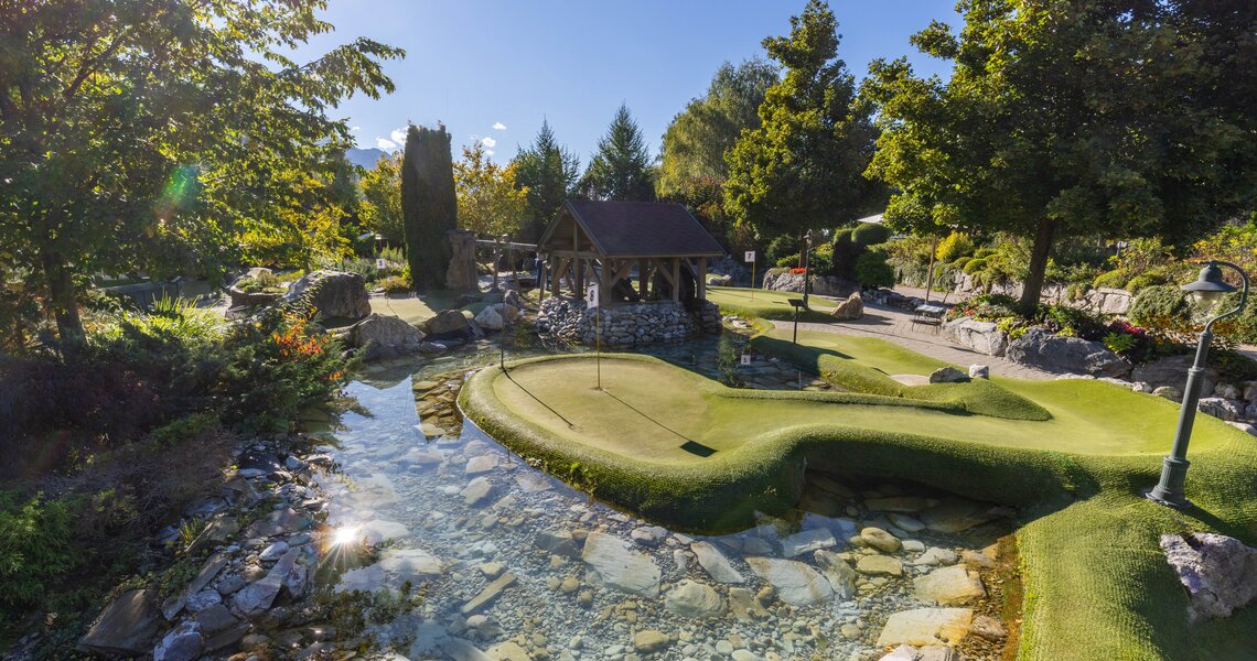 Minigolfanlage mit Wasserlauf, Brücke und Gartenlandschaft unter sonnigem Himmel. | © Leading Camping & Holiday Resort Sportcamp Woferlgut_Conny Faistauer