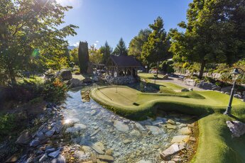 Minigolfanlage mit Wasserlauf, Brücke und Gartenlandschaft unter sonnigem Himmel. | © Leading Camping & Holiday Resort Sportcamp Woferlgut_Conny Faistauer