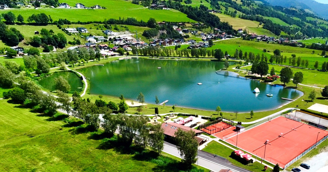 Badesee Uttendorf umgeben von grüner Landschaft mit Tennisplatz. | © TVB Uttendorf