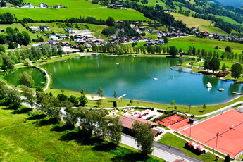 Badesee Uttendorf umgeben von grüner Landschaft mit Tennisplatz. | © TVB Uttendorf