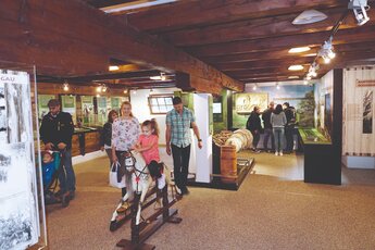Familie im Norikermuseum Niedernsill, Kind auf Holzpferd und Besucher bei Ausstellung. | © Allmayer Gerd