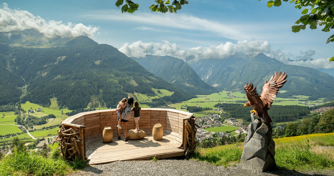 Aussichtsplattform mit Familie und Adlerfigur mit Blick über Tal, Berge und Ortschaft. | © © Wildkogel-Arena Neukirchen & Bramberg