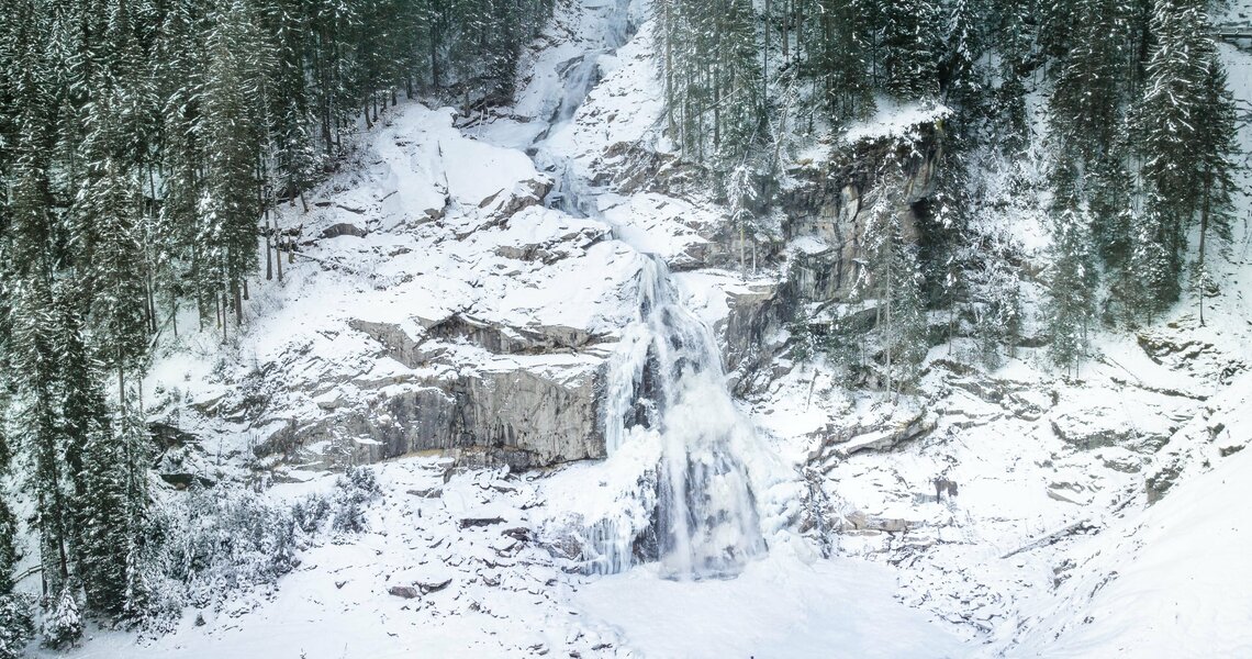Verschneite Krimmler Wasserfälle umgeben von dichten Tannenwäldern mit einer Person im Vordergrund. | © Daniel Breuer