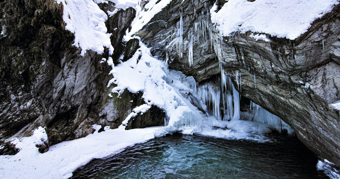 Frozen waterfall in a snowy rocky landscape with a clear water pool in the foreground. | © Rieder