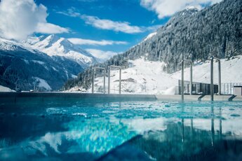 Außenpool mit Blick auf verschneite Berge und Skipisten unter klarem, blauem Himmel. | © Steinabuer Photography