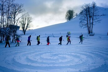 Gruppe von Schneeschuhwanderern in einer verschneiten Landschaft mit einem im Schnee gezeichneten Labyrinth. | © Florian Kreidl Glück