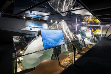 Ausstellung mit Bergmodell, Spiegeldecke und Bildschirmen, die Naturaufnahmen zeigen | © zangl.ultd-Franz Neumayr-Leo