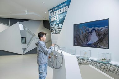Junge erkundet interaktive Gletscherwelt mit Steuerrad und digitaler Darstellung eines Gletschers. | © zangl.ultd - Franz Neumayr - Leo