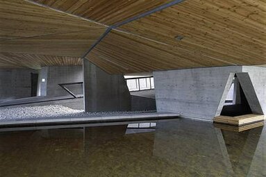 Überdachter Außenbereich mit Holzdecke, Betonwänden und einem reflektierenden Wasserbecken. | © Nationalparkzentrum Hohe Tauern GmbH