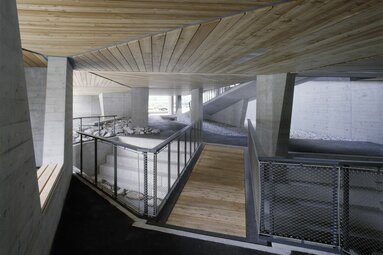 Überdachter Bereich mit Holzdecke, Betonpfeilern, Geländern und Wegen aus Holz und Stein. | © Paul Ott
