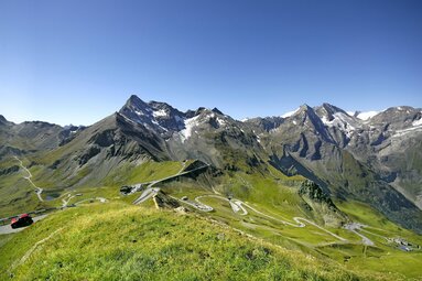 Panorama der Großglockner-Hochalpenstraße mit Kurven, grünen Wiesen und Berggipfeln. | © Großglockner - Woeckinger