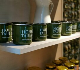 Grüne Tassen mit der Aufschrift "Hohe Tauern" stehen auf einem weißen Regal. | © Nationalparkzentrum Hohe Tauern GmbH