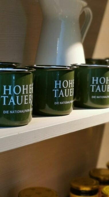 Grüne Tassen mit der Aufschrift "Hohe Tauern" stehen auf einem weißen Regal. | © Nationalparkzentrum Hohe Tauern GmbH