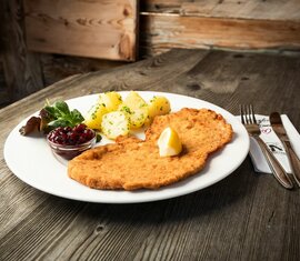 Teller mit Wiener Schnitzel, Kartoffeln, Preiselbeeren und Salat auf einem Holztisch | © SalzburgerLand Tourismus 