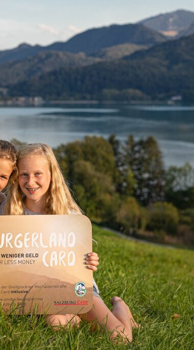 Zwei Mädchen halten ein Schild mit der SalzburgerLand Card vor einer Seelandschaft | © SalzburgLand Tourismus - Michael Grössinger