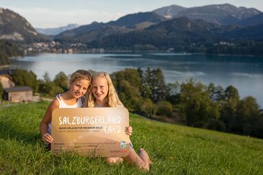 Zwei Mädchen halten ein Schild mit der SalzburgerLand Card vor einer Seelandschaft | © SalzburgLand Tourismus - Michael Grössinger