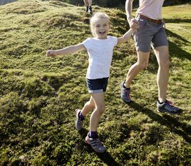 Familie beim Wandern auf einer Wiese, Tochter lacht und hält die Hand der Mutter | © SalzburgLand Tourismus