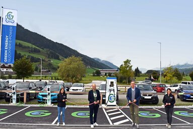 Eröffnung einer Ladestation für Elektroautos mit vier Personen und Berglandschaft im Hintergrund.