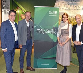 Vier Personen beim Hohe Tauern Tourismustag, vor einem Banner und alpiner Hintergrundkulisse. | © Ferienregion Nationalpark Hohe Tauern