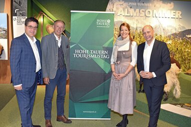 Vier Personen beim Hohe Tauern Tourismustag, vor einem Banner und alpiner Hintergrundkulisse. | © Ferienregion Nationalpark Hohe Tauern