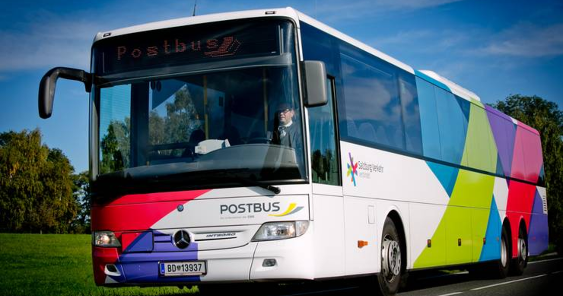 Postbus fährt auf einer Straße mit buntem Design und Fahrer sichtbar im Cockpit. | © Salzburger Verkehrsverbund GmbH