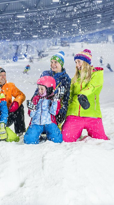 Fröhliche Familie in bunter Winterkleidung genießt den Schnee in einer Skihalle.