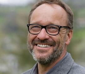 Lächelnder Mitarbeiter von der Nationalparkverwaltung Hohe Tauern in Salzburg mit Brille vor Naturkulisse. | © NPHT / A. Baldinger