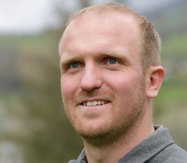Mitarbeiter der Nationalparkverwaltung Hohe Tauern in Salzburg, im grauen Gilet vor grüner Naturkulisse. | © Nationalparkverwaltung Salzburg