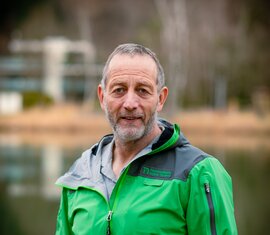 Mitarbeiter von der Nationalparkverwaltung Hohe Tauern in Salzburg, in Nationalparkjacke vor ruhigem See. | © NPHT / Kreidl & Glück