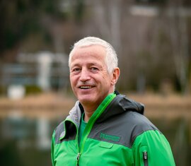 Lächelnder Mitarbeiter von der Nationalparkverwaltung Hohe Tauern in Salzburg, in Nationalparkjacke am See. | © NPHT / Kreidl & Glück