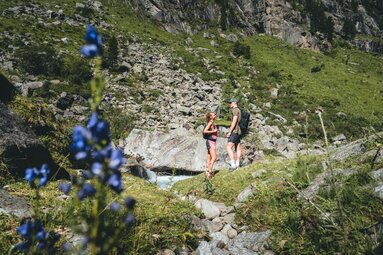 Paar steht an einem Gebirgsbach, umgeben von Felsen und Wiesen. | © Ferienregion Nationalpark Hohe Tauern - Daniel Kogler