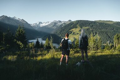 Zwei Wanderer genießen den Blick auf einen Stausee und Gletscher in den Alpen. | © Ferienregion Nationalpark Hohe Tauern - Daniel Kogler